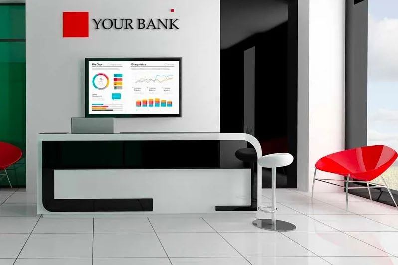 Empfangstresen einer Bank mit einem Bildschirm an der Wand, der Diagramme zeigt