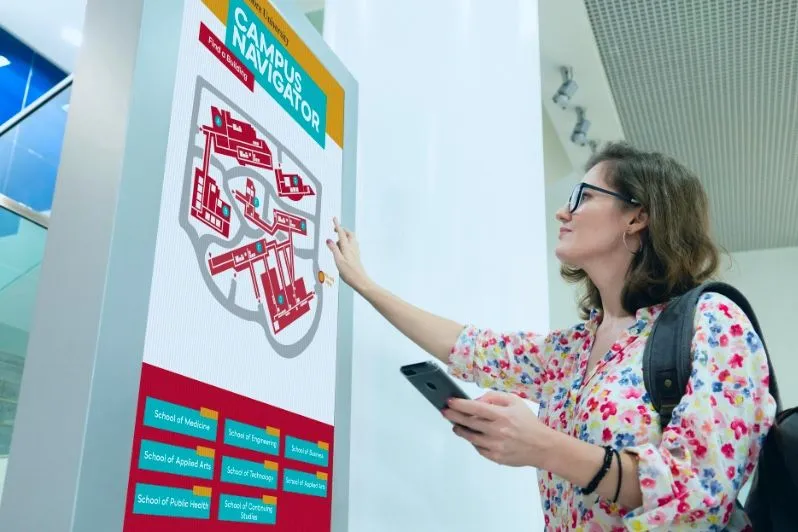 Studentin nutzt einen interaktiven Campusplan auf einem Touchscreen