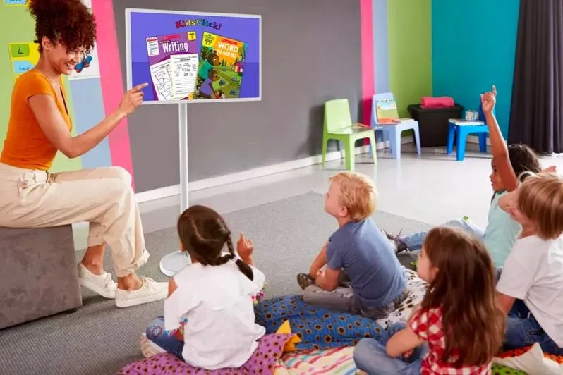 Lehrerin und Kinder in einem Klassenraum mit einem Bildschirm auf einem Ständer
