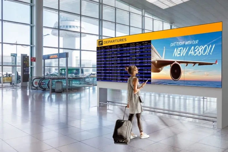 Reisender mit Koffer vor einer Abflugtafel am Flughafen