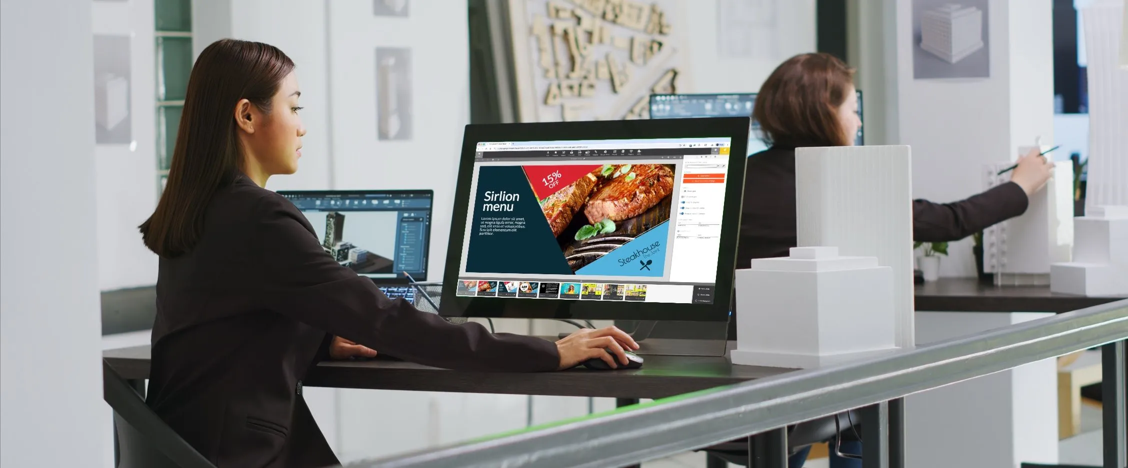 Frau gestaltet im Play-Editor an einem Desktop-Monitor eine Folie mit der Speisekarte eines Steakhauses